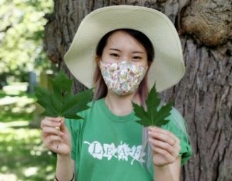 Woman wearing a face masks holds up two maple leaves