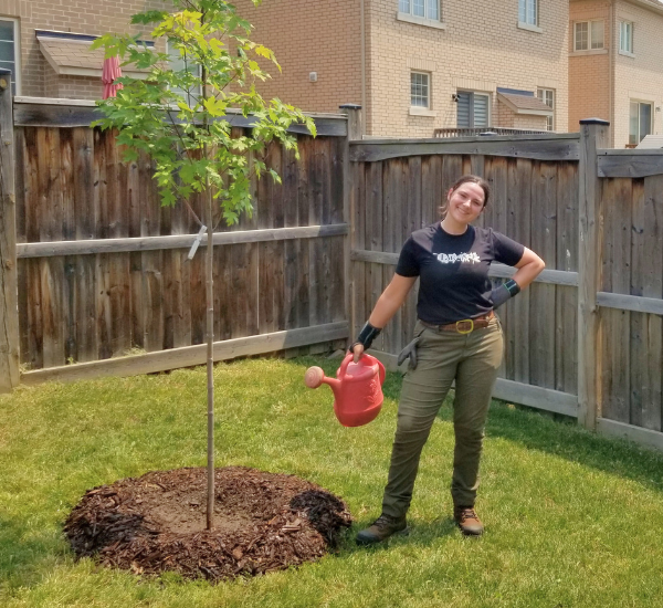 Residential Planting Program Assistant, Amba, posing next to a newly planted tree.(© Brenna Anstett / LEAF)