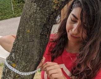 Young woman measuring the width of a tree trunk with measuring tape