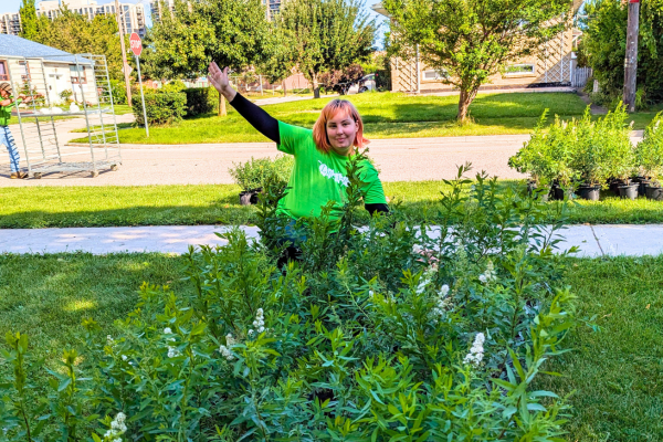 Naomi in a green LEAF shirt standing behind the shrubs she helped distribute at the Dorset Park Tree Tour.