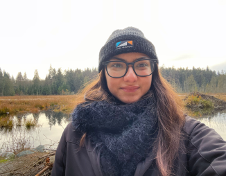 A person standing in front of a wetland ecosystem, a forest in the background