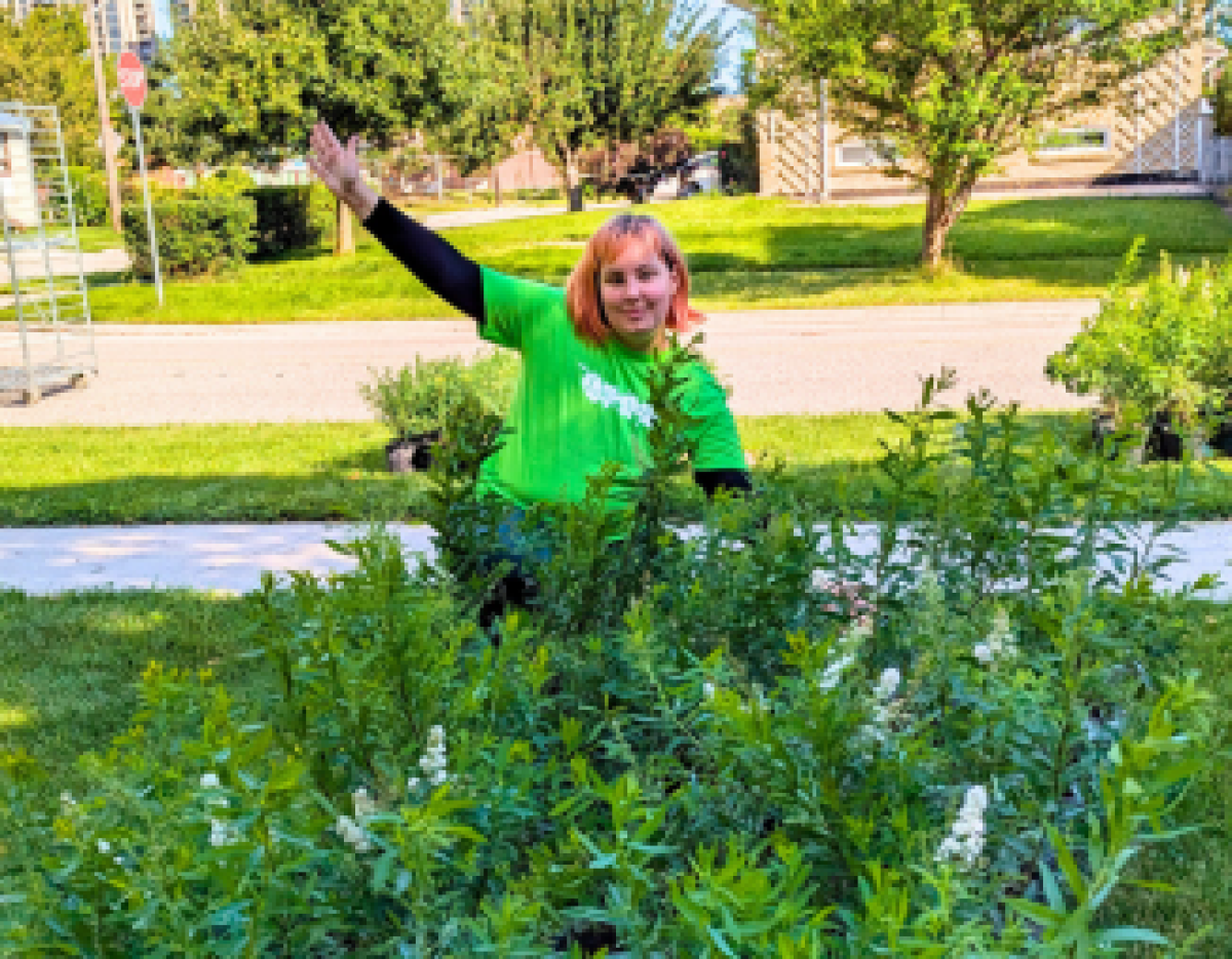 Naomi in a green LEAF shirt standing behind the shrubs she helped distribute at the Dorset Park Tree Tour.