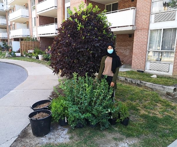 Aisha standing with shrubs in front of building(©2021 James Marcucci / LEAF)