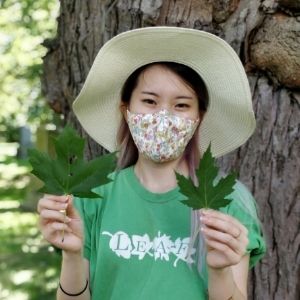 Woman wearing a face mask holds up two maple leaves