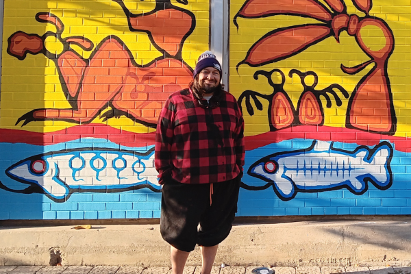 Ojibway Woodland artist Thomas Sinclair posing with his mural, located at the Bathurst Station Urban Forest Demonstration Garden
